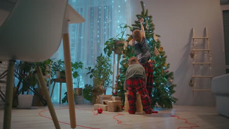 Two-brothers-in-pajamas-decorate-the-Christmas-ball-in-the-living-room-of-the-house-on-Christmas-Eve.-High-quality-4k-footage